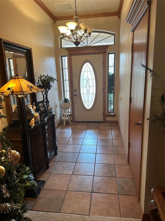 entryway with crown molding, light tile patterned floors, and an inviting chandelier