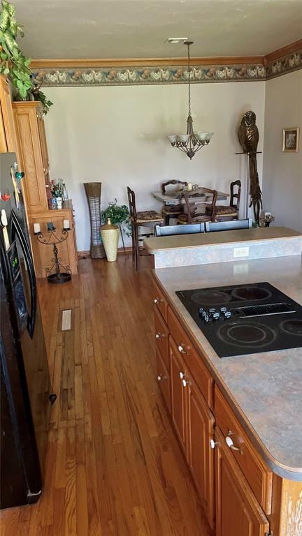kitchen with an inviting chandelier, brown cabinets, wood-type flooring, black appliances, and hanging light fixtures