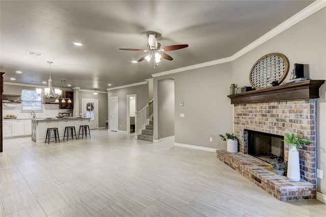 living room with ceiling fan with notable chandelier, ornamental molding, and a fireplace