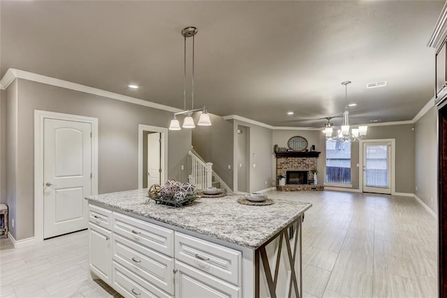 kitchen with a brick fireplace, light stone counters, decorative light fixtures, a center island, and white cabinetry