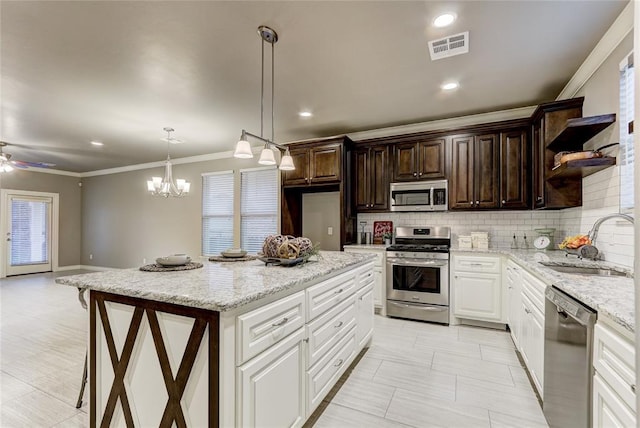 kitchen with stainless steel appliances, sink, white cabinets, a center island, and hanging light fixtures