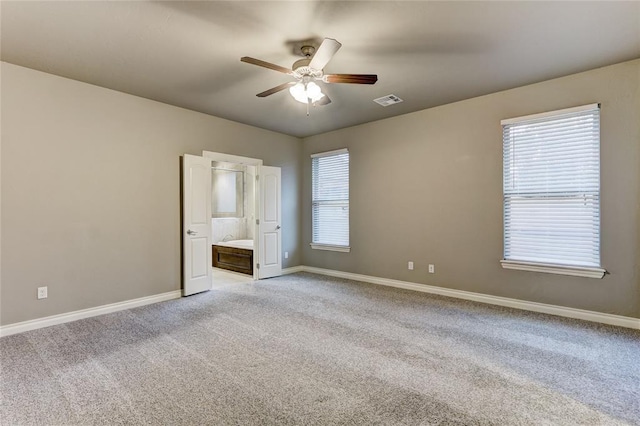 unfurnished bedroom featuring multiple windows, ensuite bathroom, ceiling fan, and light colored carpet