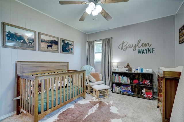 carpeted bedroom featuring ceiling fan, wood walls, and a crib