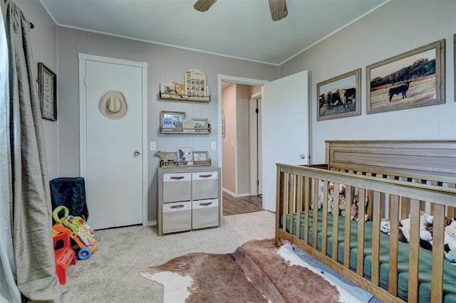 carpeted bedroom featuring ceiling fan and a crib