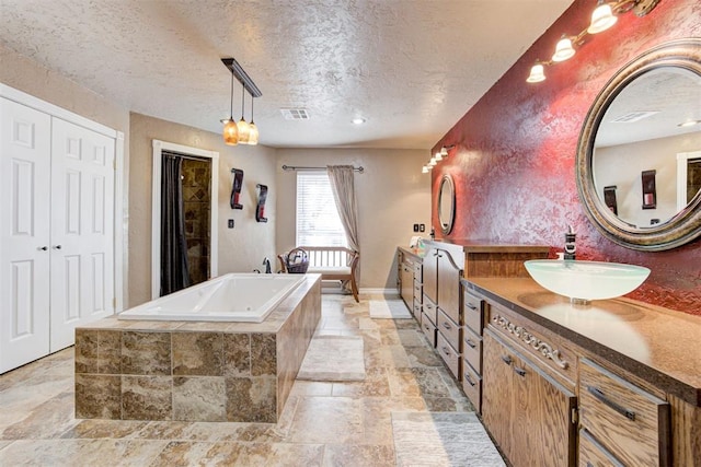 bathroom featuring vanity, a textured ceiling, and tiled tub