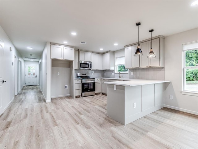 kitchen with pendant lighting, light hardwood / wood-style flooring, appliances with stainless steel finishes, backsplash, and kitchen peninsula