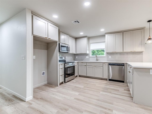 kitchen with pendant lighting, backsplash, light wood-type flooring, and appliances with stainless steel finishes