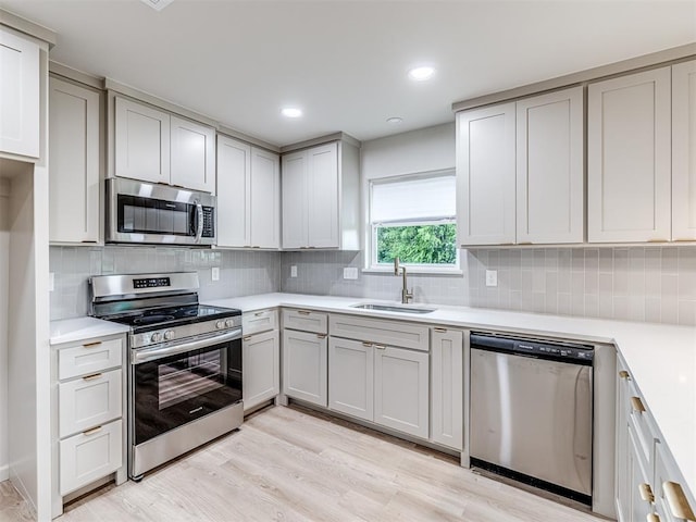 kitchen with tasteful backsplash, sink, stainless steel appliances, and light hardwood / wood-style floors