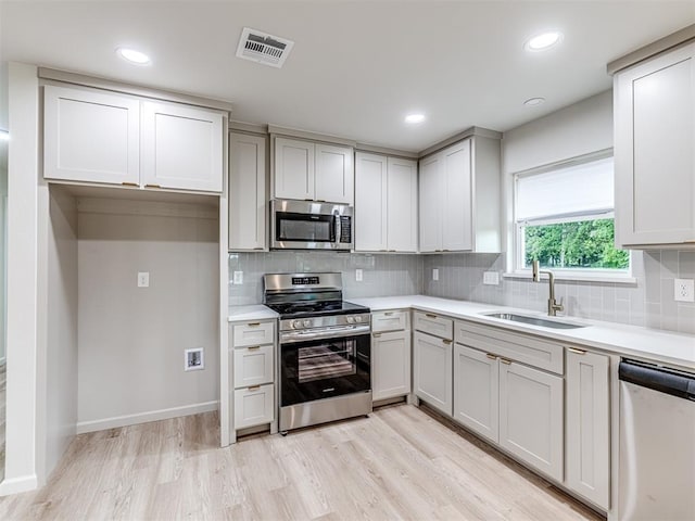 kitchen with stainless steel appliances, sink, decorative backsplash, and light hardwood / wood-style flooring