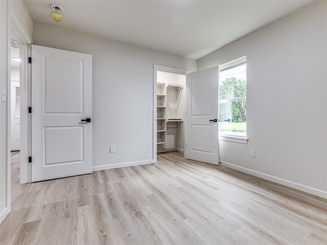 unfurnished bedroom featuring a walk in closet, a closet, and light hardwood / wood-style flooring