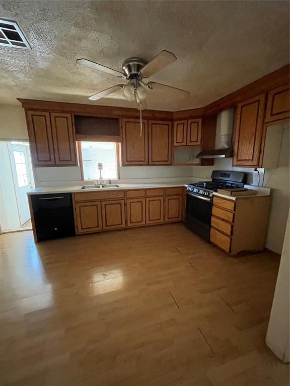 kitchen with wall chimney exhaust hood, gas range oven, ceiling fan, black dishwasher, and light hardwood / wood-style floors