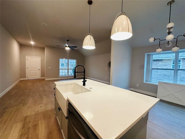 kitchen featuring dishwasher, light countertops, hanging light fixtures, and a kitchen island with sink