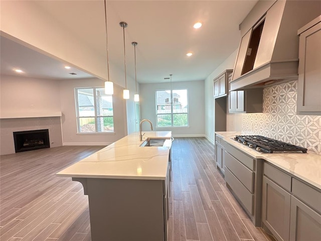 kitchen with dark hardwood / wood-style flooring, premium range hood, light stone counters, sink, and an island with sink