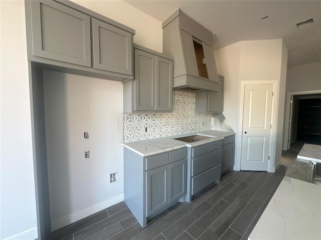 kitchen featuring gray cabinetry, light stone countertops, tasteful backsplash, premium range hood, and black electric cooktop