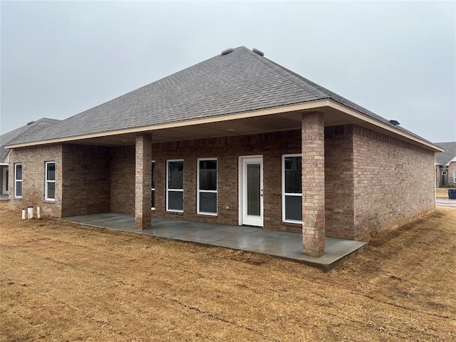 back of property with brick siding, a shingled roof, a lawn, and a patio area