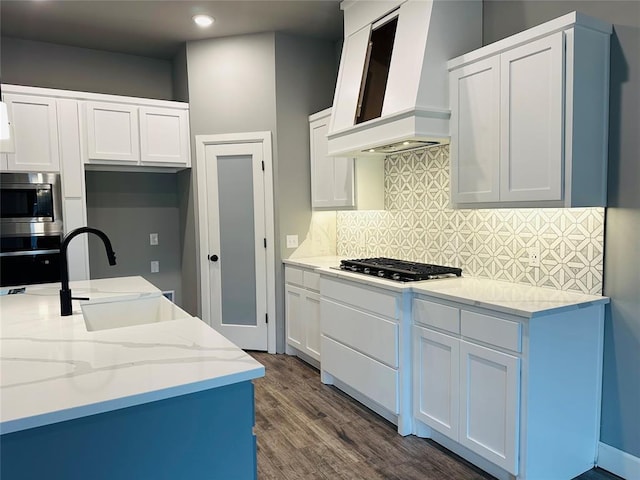 kitchen featuring wall chimney range hood, light stone counters, white cabinets, stainless steel appliances, and a sink