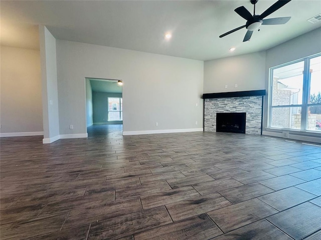 unfurnished living room with dark hardwood / wood-style flooring, a stone fireplace, a wealth of natural light, and ceiling fan