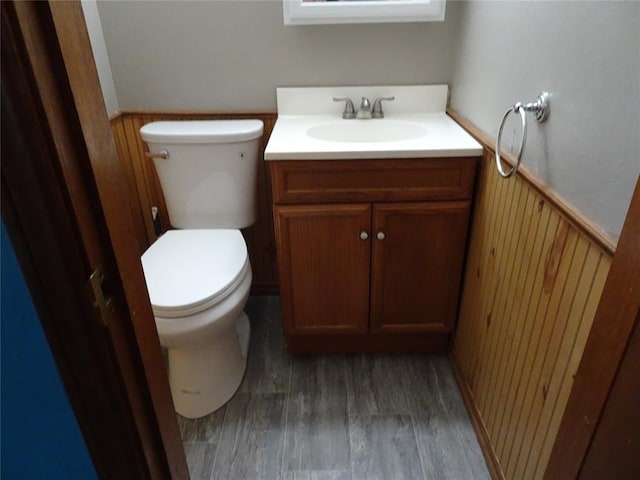 bathroom featuring vanity, hardwood / wood-style floors, wood walls, and toilet