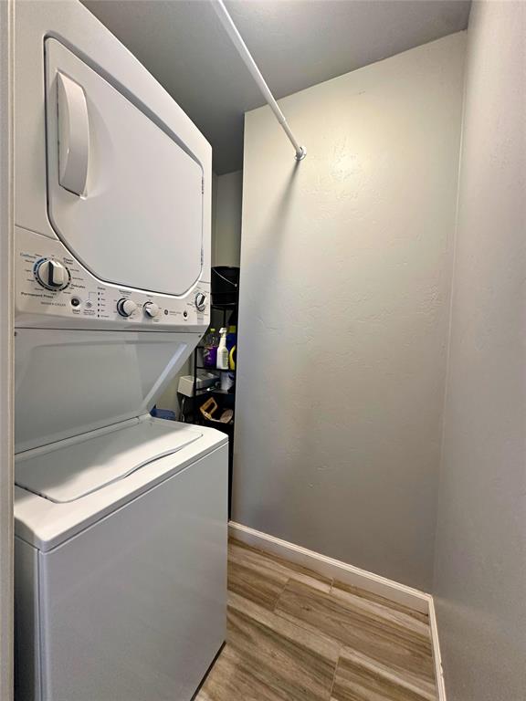 laundry area with stacked washer / drying machine and light wood-type flooring