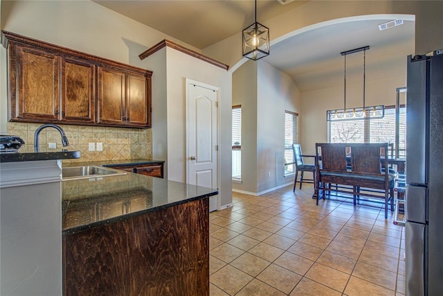 kitchen featuring light tile patterned flooring, dark stone countertops, tasteful backsplash, stainless steel refrigerator, and pendant lighting