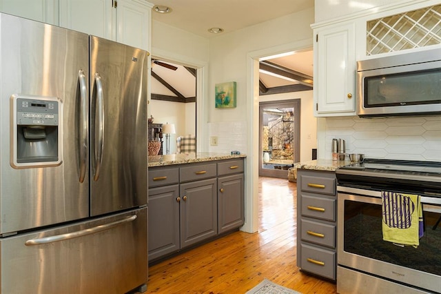 kitchen with gray cabinetry, backsplash, white cabinets, light stone counters, and stainless steel appliances