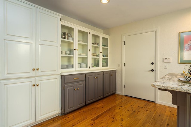 kitchen with light stone countertops, gray cabinets, dark hardwood / wood-style floors, and white cabinetry