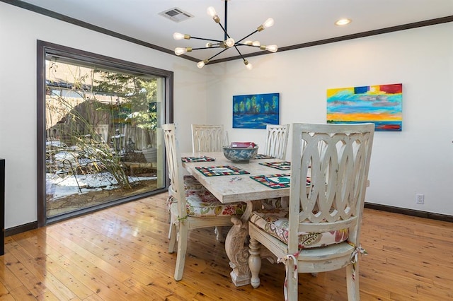 dining area with light wood-type flooring, ornamental molding, and a notable chandelier