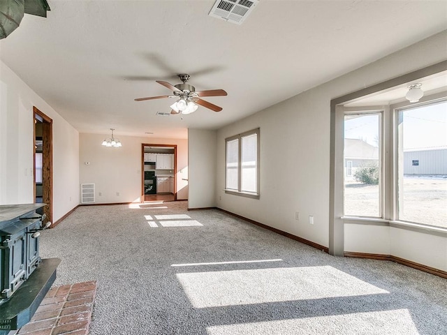 unfurnished living room with ceiling fan with notable chandelier, a wood stove, and carpet