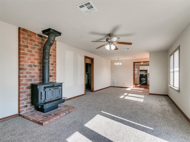 unfurnished living room featuring ceiling fan with notable chandelier, a wood stove, and carpet