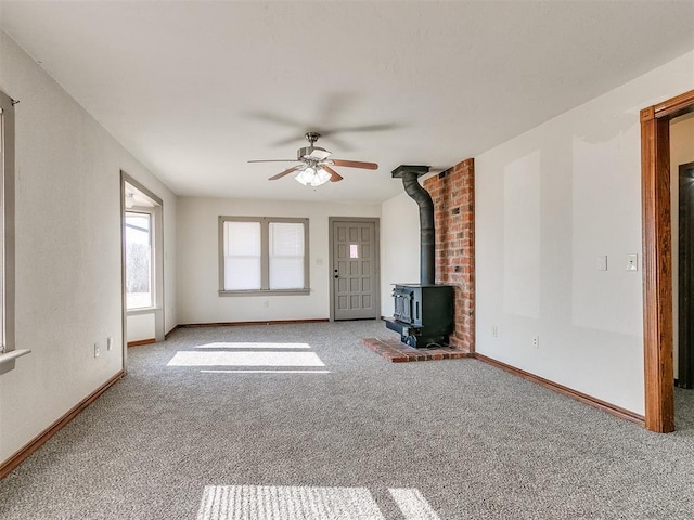 unfurnished living room featuring ceiling fan, light carpet, and a wood stove