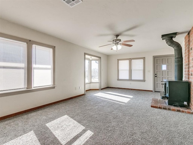 unfurnished living room featuring carpet flooring, ceiling fan, and a wood stove