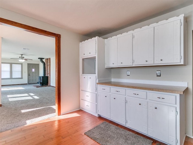 kitchen featuring white cabinets, ceiling fan, light hardwood / wood-style flooring, and a wood stove