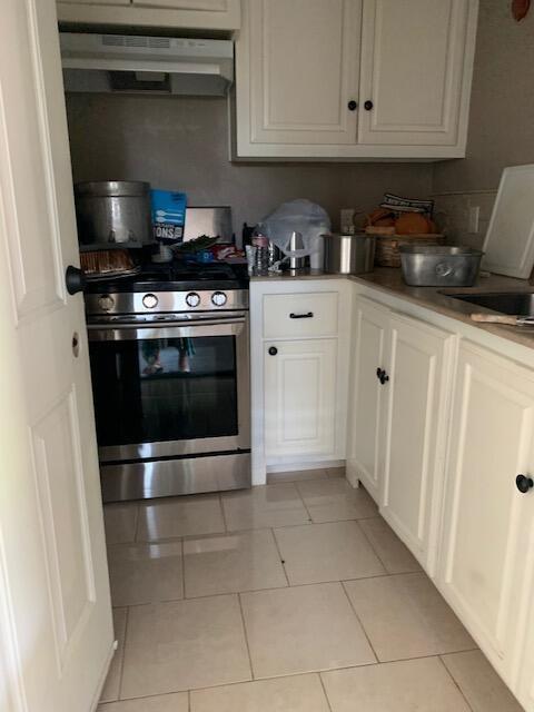 kitchen with white cabinets, stainless steel stove, exhaust hood, and light tile patterned floors