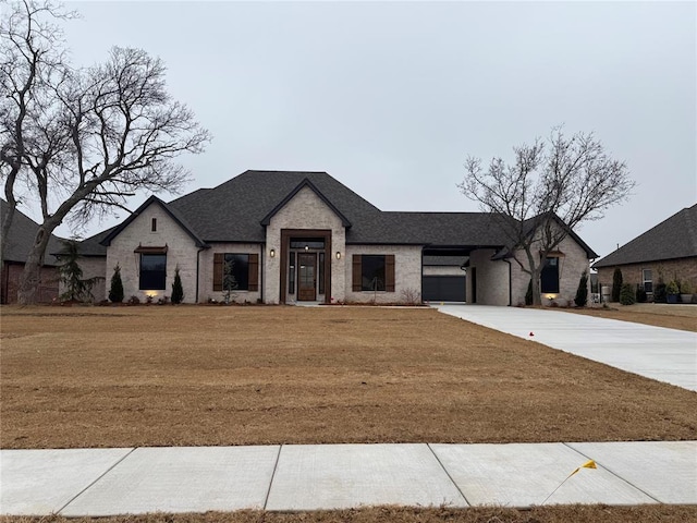 view of front of home featuring driveway, brick siding, a front lawn, and roof with shingles