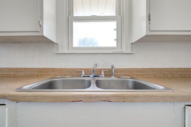 interior details with backsplash, sink, and white cabinetry