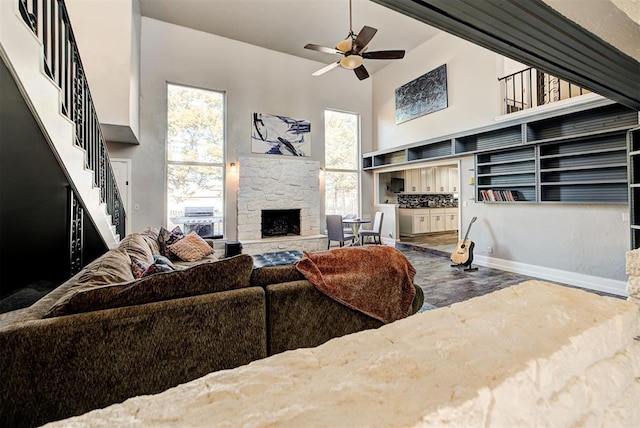 living room with ceiling fan, wood-type flooring, a fireplace, and a high ceiling