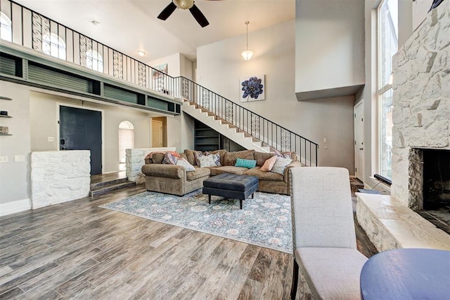 living room with hardwood / wood-style floors, a towering ceiling, a fireplace, and ceiling fan