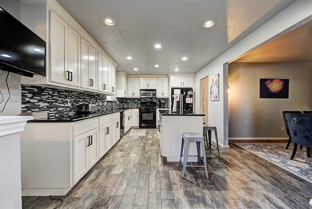 kitchen featuring a breakfast bar, white cabinetry, decorative backsplash, a center island, and black appliances