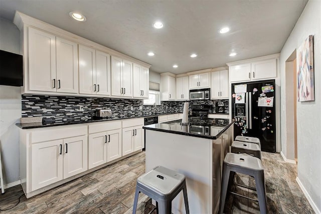 kitchen with white cabinetry, backsplash, a kitchen island, black appliances, and a kitchen bar