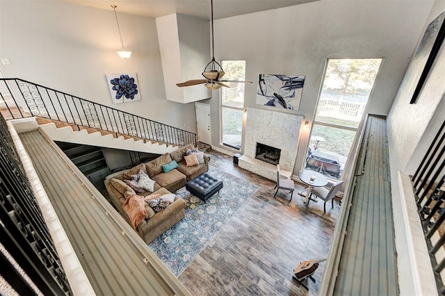 living room featuring a stone fireplace, a towering ceiling, hardwood / wood-style floors, and ceiling fan