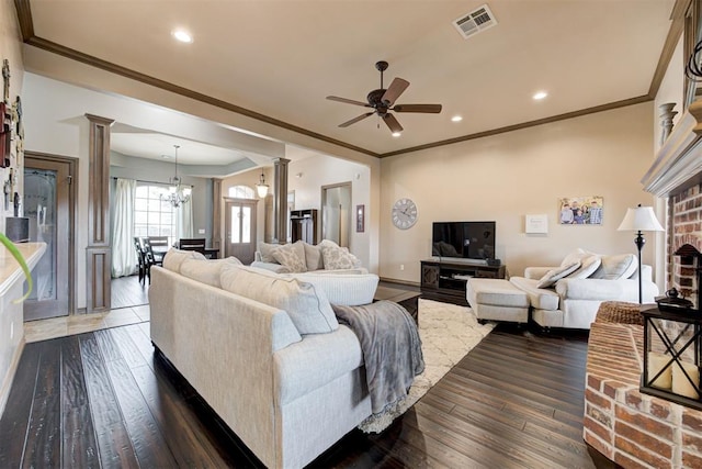 living area with visible vents, decorative columns, ceiling fan with notable chandelier, and dark wood-style flooring
