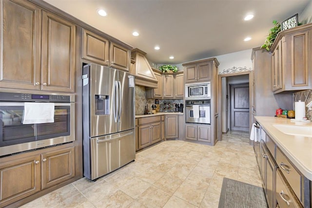kitchen with custom exhaust hood, light countertops, a sink, appliances with stainless steel finishes, and backsplash