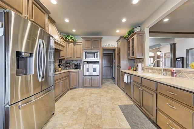 kitchen with a sink, light countertops, stainless steel appliances, tasteful backsplash, and glass insert cabinets