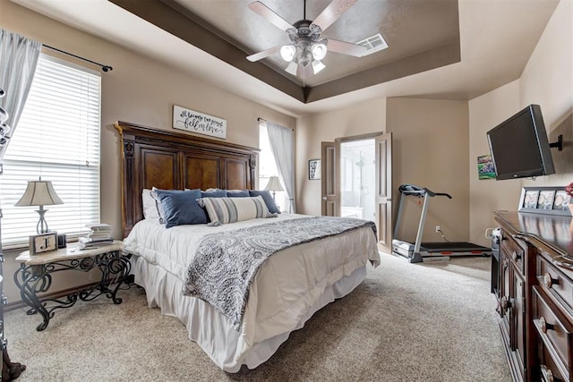 bedroom featuring visible vents, baseboards, light colored carpet, a tray ceiling, and a ceiling fan