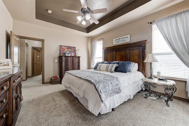 bedroom with a ceiling fan, baseboards, light colored carpet, and a raised ceiling