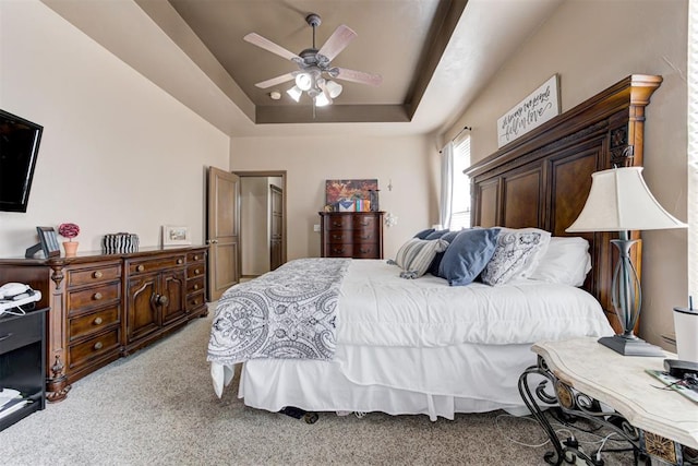 bedroom with a ceiling fan, a tray ceiling, and light carpet
