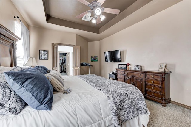 bedroom with light carpet, baseboards, a walk in closet, a tray ceiling, and a ceiling fan