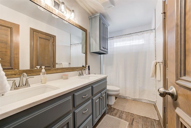 full bath with double vanity, a sink, wood finished floors, and toilet