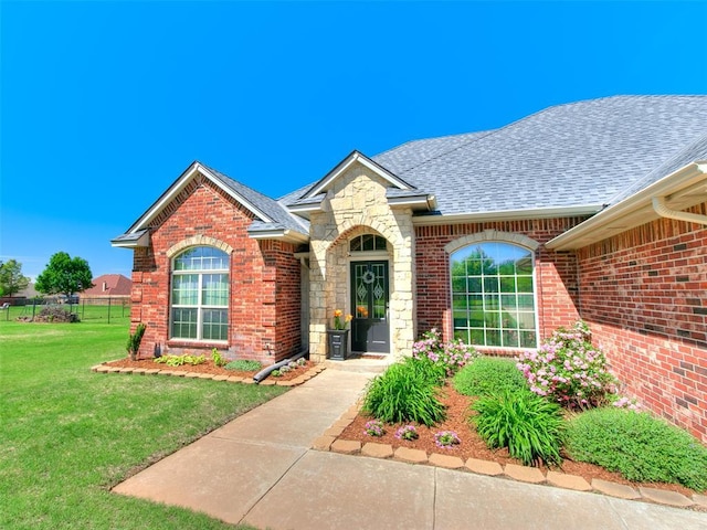 ranch-style house with roof with shingles, stone siding, brick siding, and a front yard