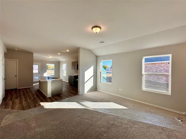 unfurnished living room with dark colored carpet, vaulted ceiling, and sink